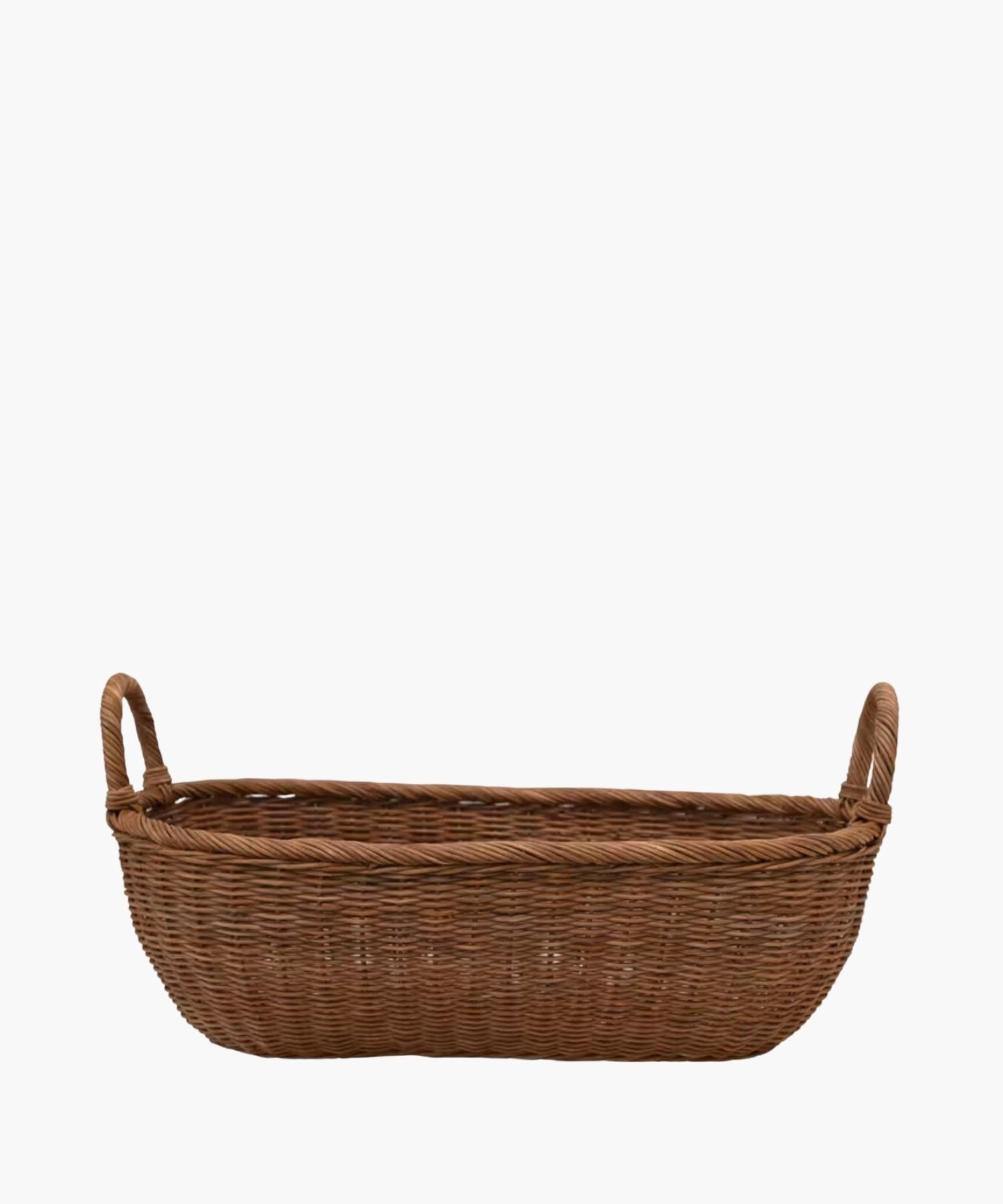 A handwoven wicker basket with two looped handles on either side featuring an organic oval shape and a natural brown finish. The basket has a natural, rustic appearance. | S.W. Home