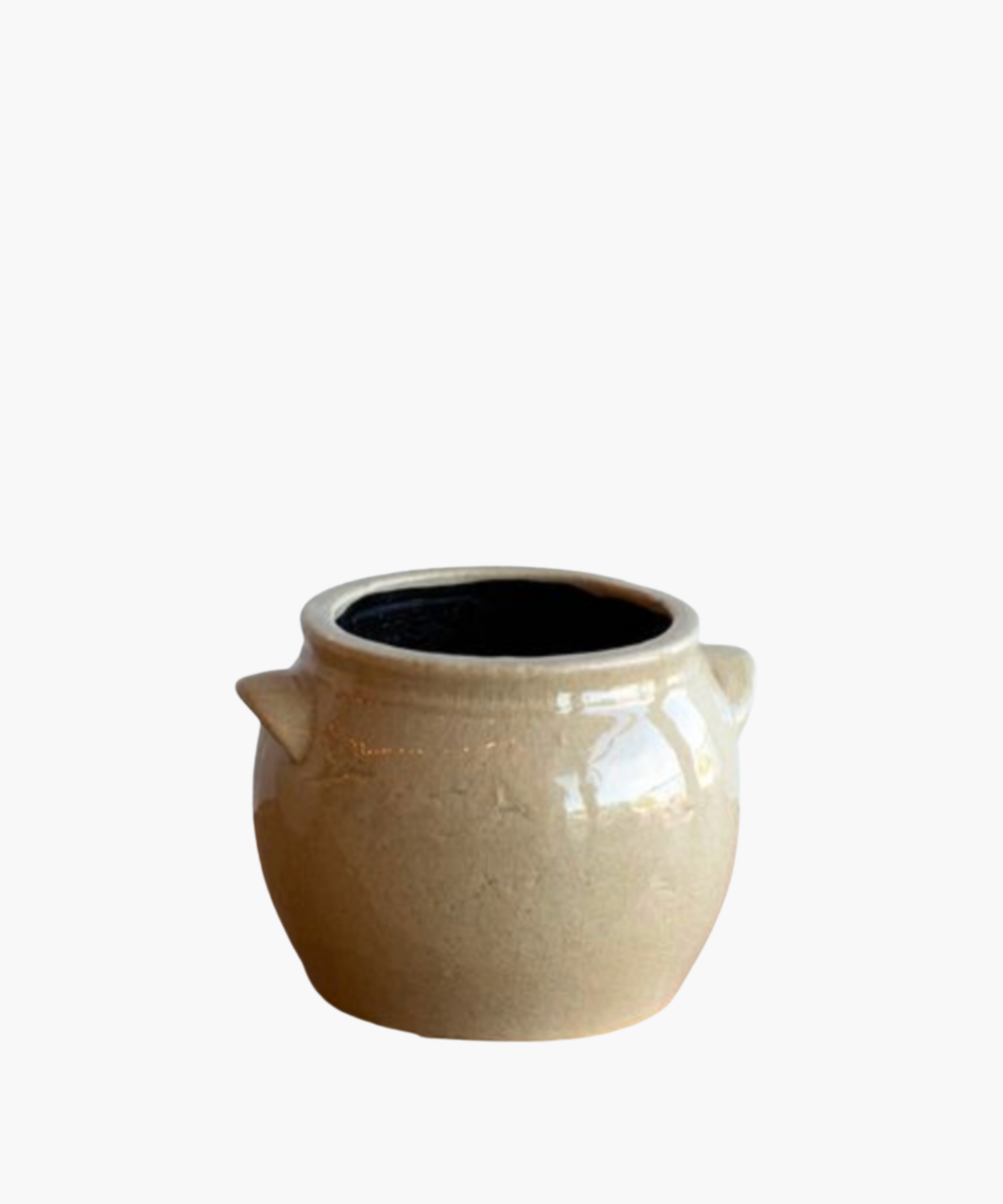 A beige ceramic pot with a glossy finish, featuring two small side handles and a black interior. The pot has a smooth, rounded shape and exudes a rustic charm. | S.W. Home