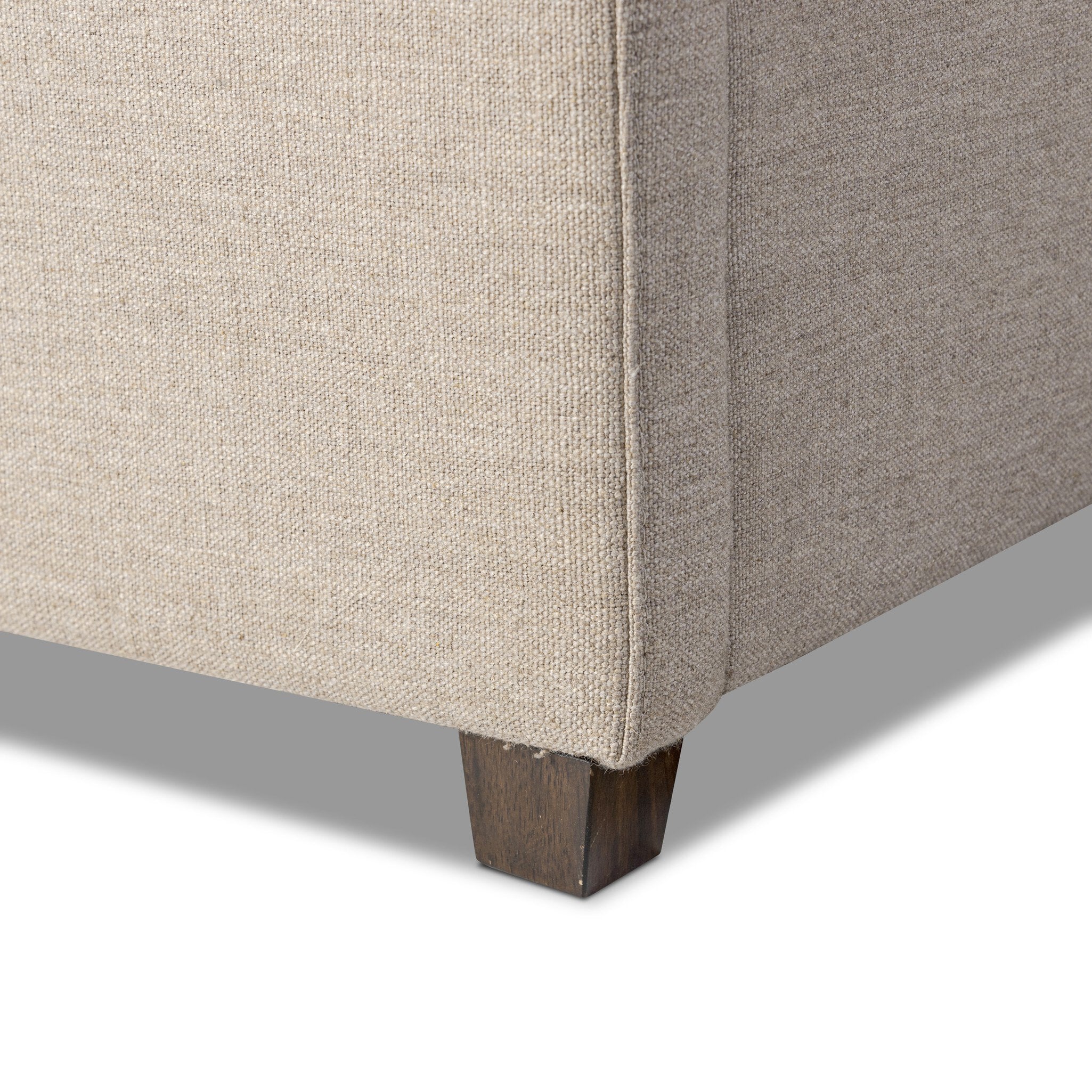 Close up of a taupe upholstered bed with horizontal channeling on the headboard and white bedding on a white background.