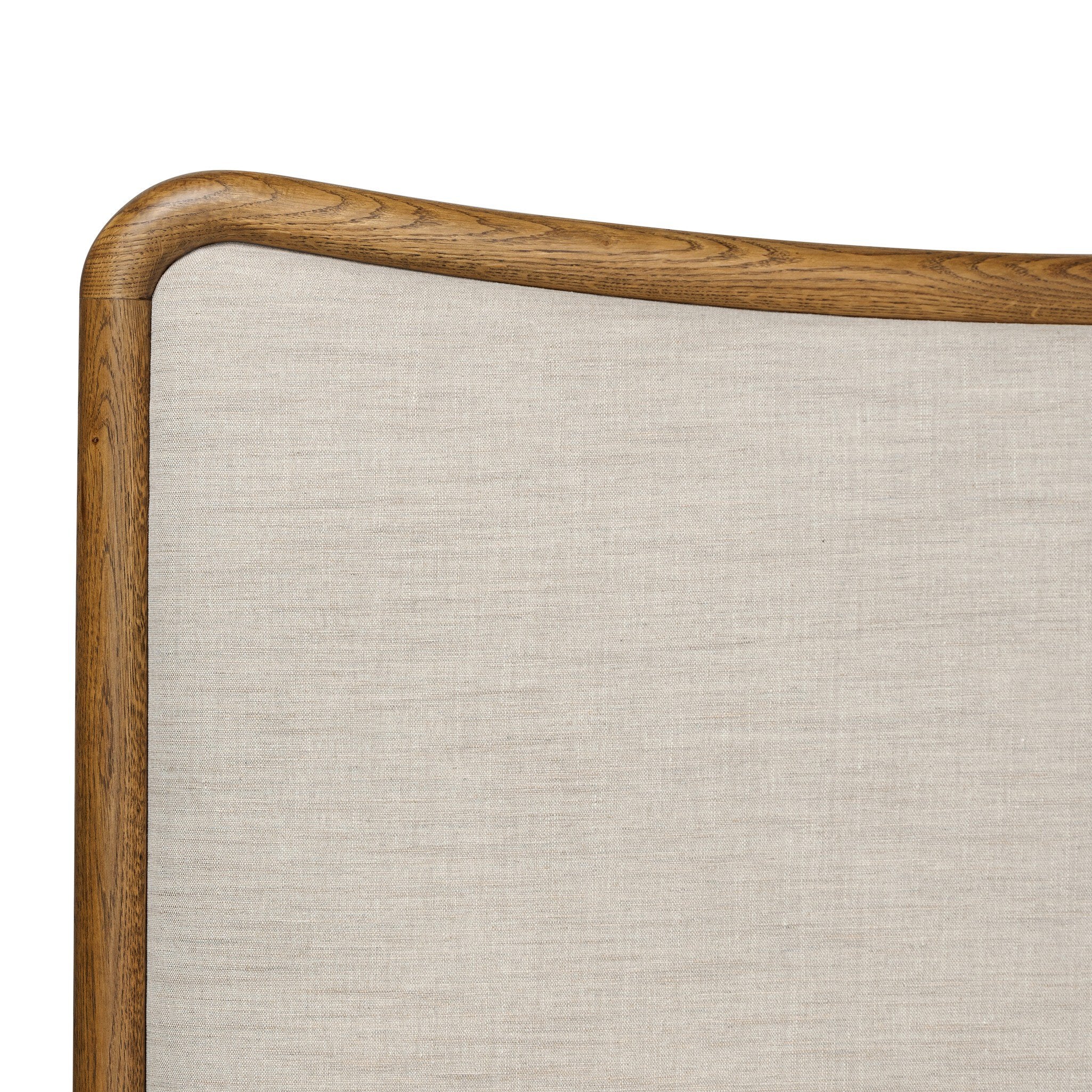 Close up of a heritage-inspired oak bed featuring soft curves, linen upholstered headboard, and white bedding on a white background.