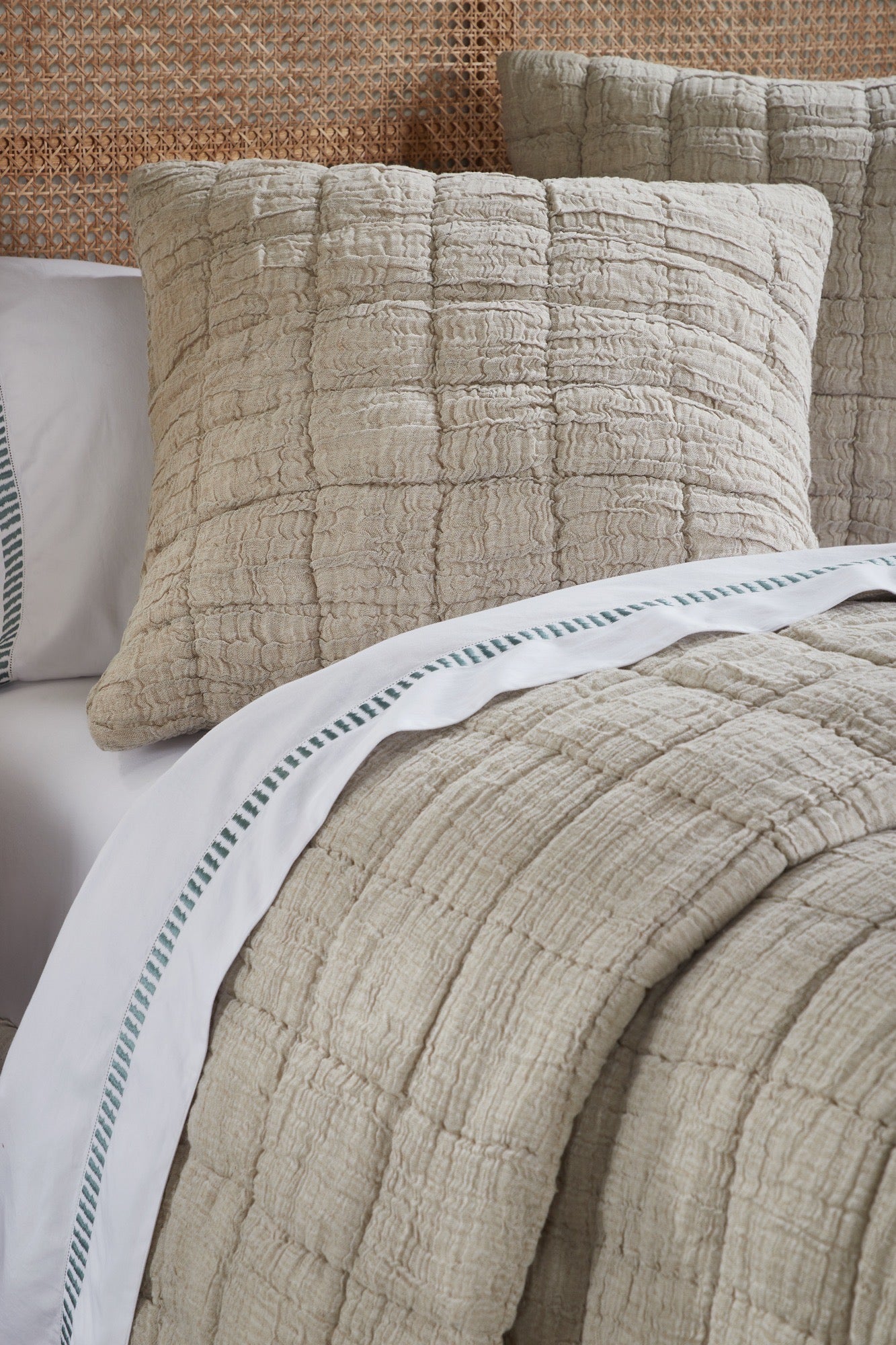 A bed styled with a beige cotton-linen quilt and shams layered atop cream bedding with hand-stitched texture and relaxed elegance. | Wildwood Home Co.