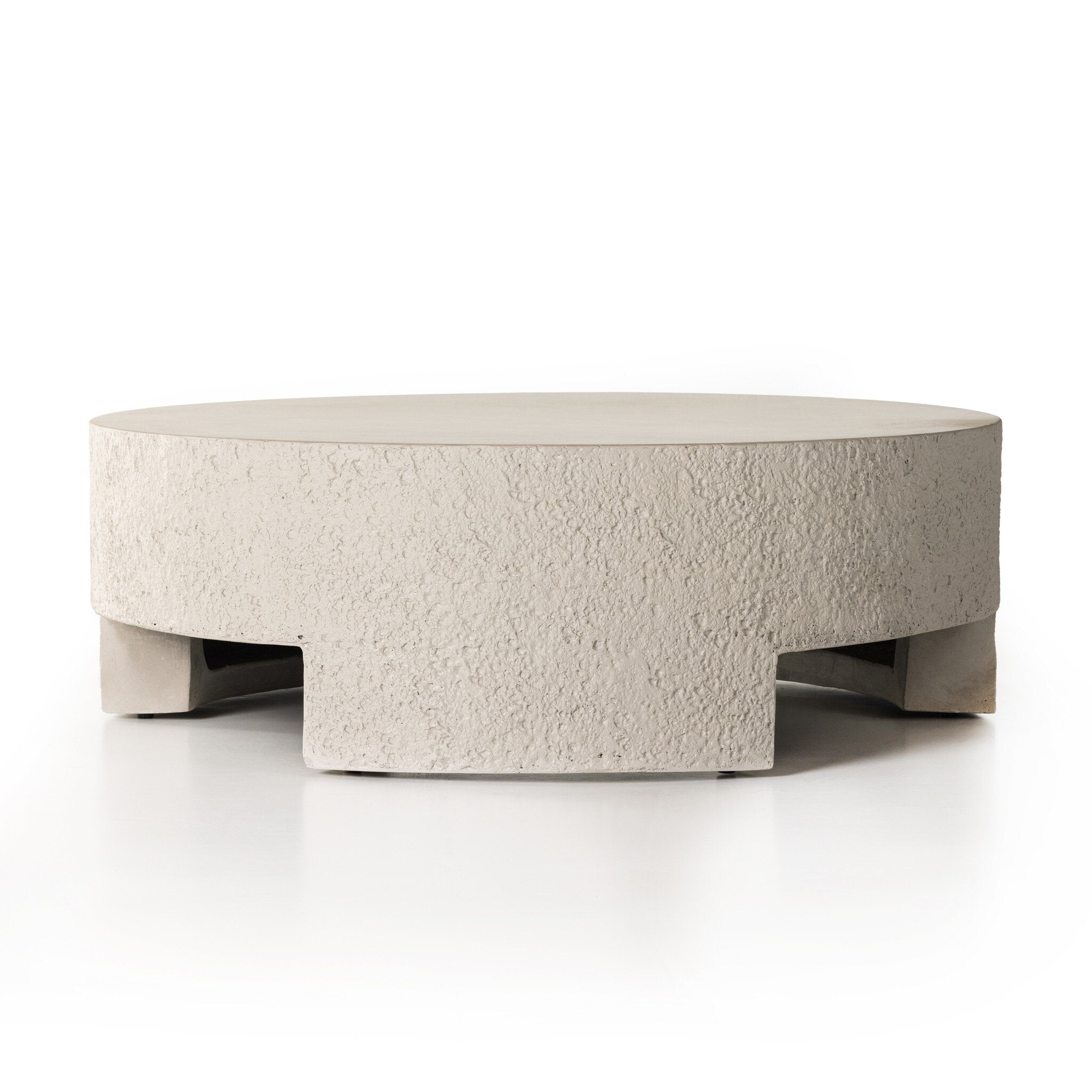 A round pumice concrete coffee table with a smooth top and cutout legs. | S.W. Home