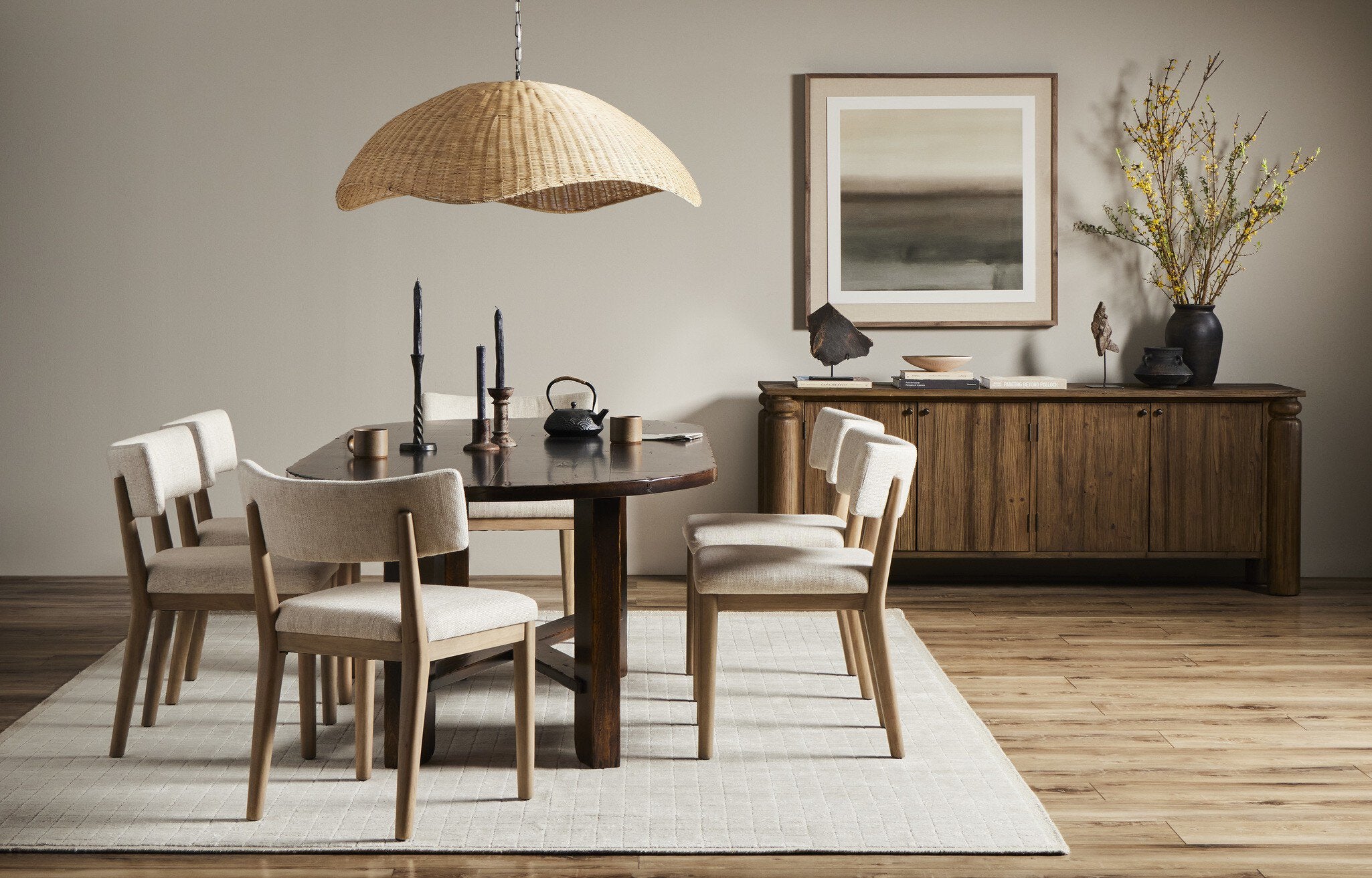 Dining room with wooden table and chairs, woven pendant light, and abstract painting.