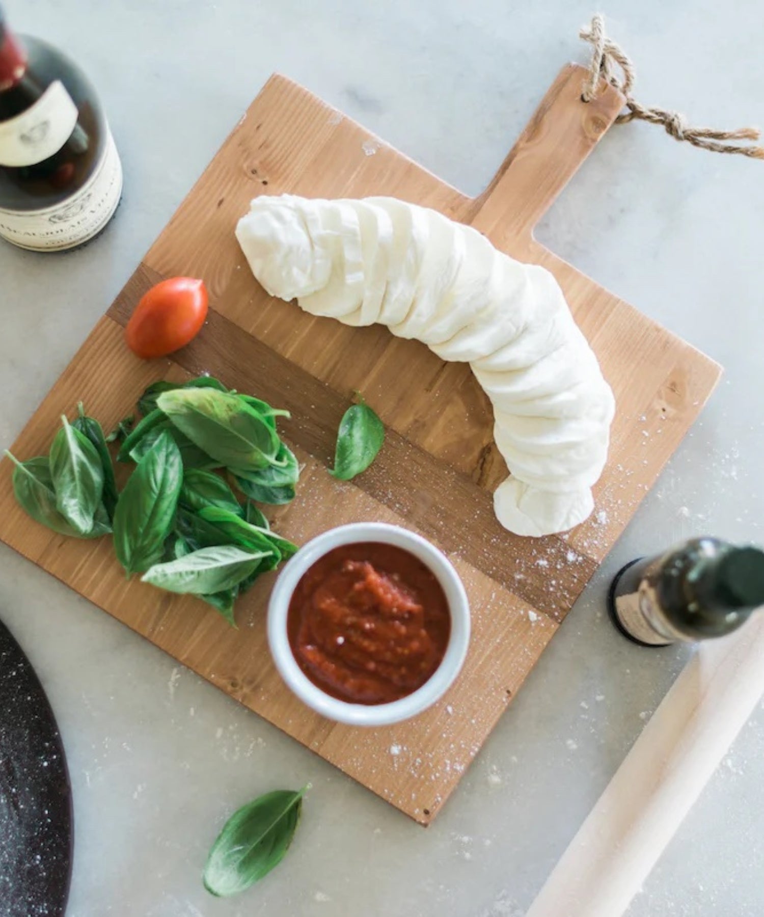Square pine wood cutting or charcuterie board with a natural finish, featuring a dark horizontal stripe and a handle with a rope loop styled with cheese and wine. | SW Home