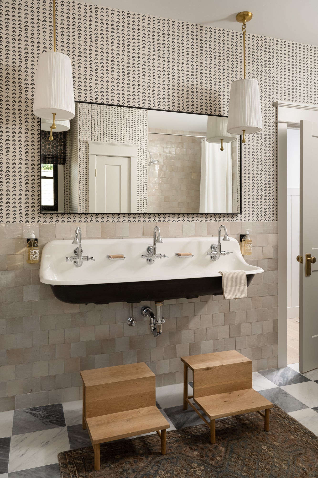 Stylish bathroom with decorative wallpaper, a vintage triple sink, wooden step stools, and elegant pendant lights, conveying a cozy, retro vibe. | Wildwood Home Co.