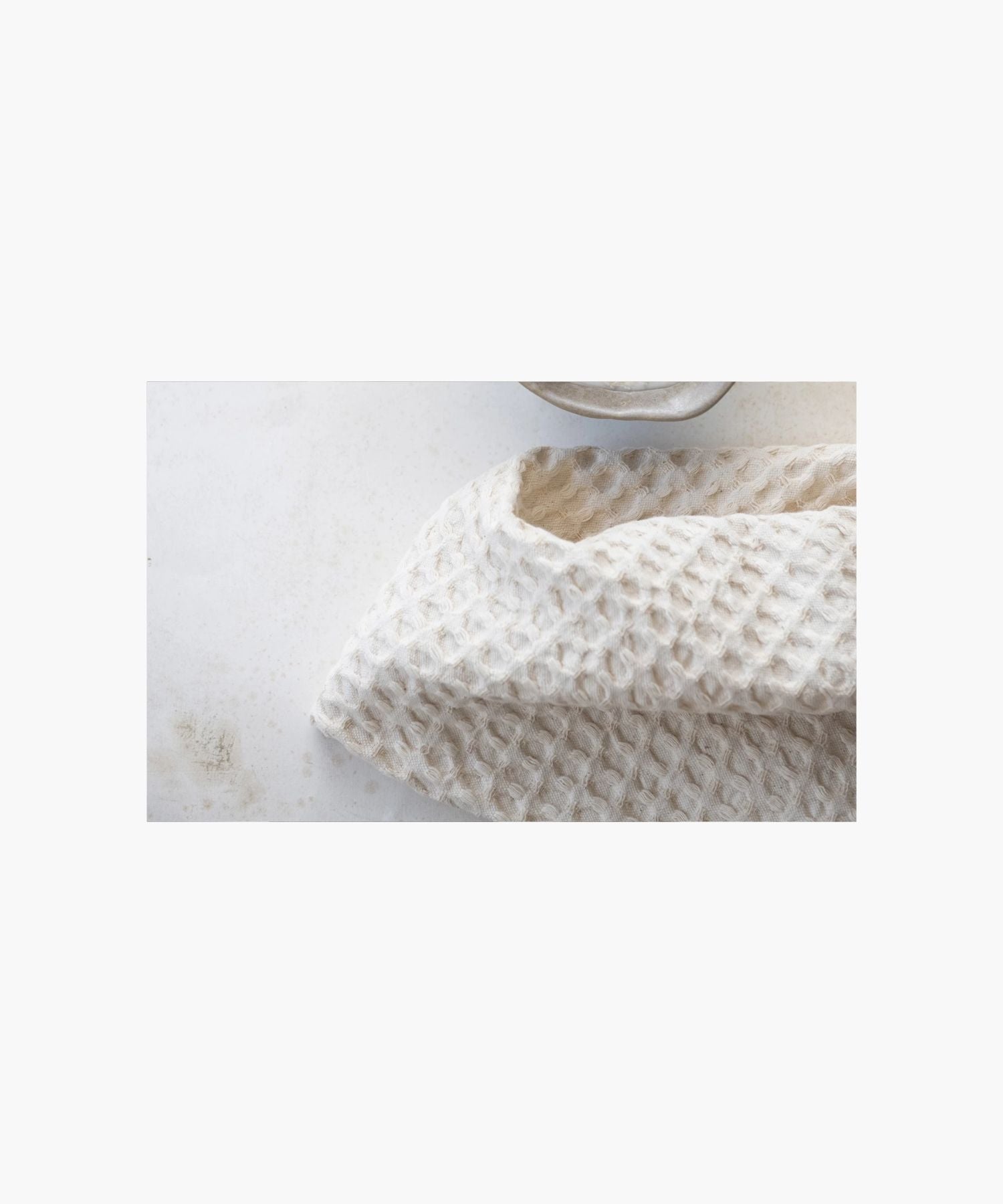 A cream colored, rectangular waffle-weave tea towel styled on a marble counter highlighting the texture and a clean, simple appearance. | Wildwood Home Co.