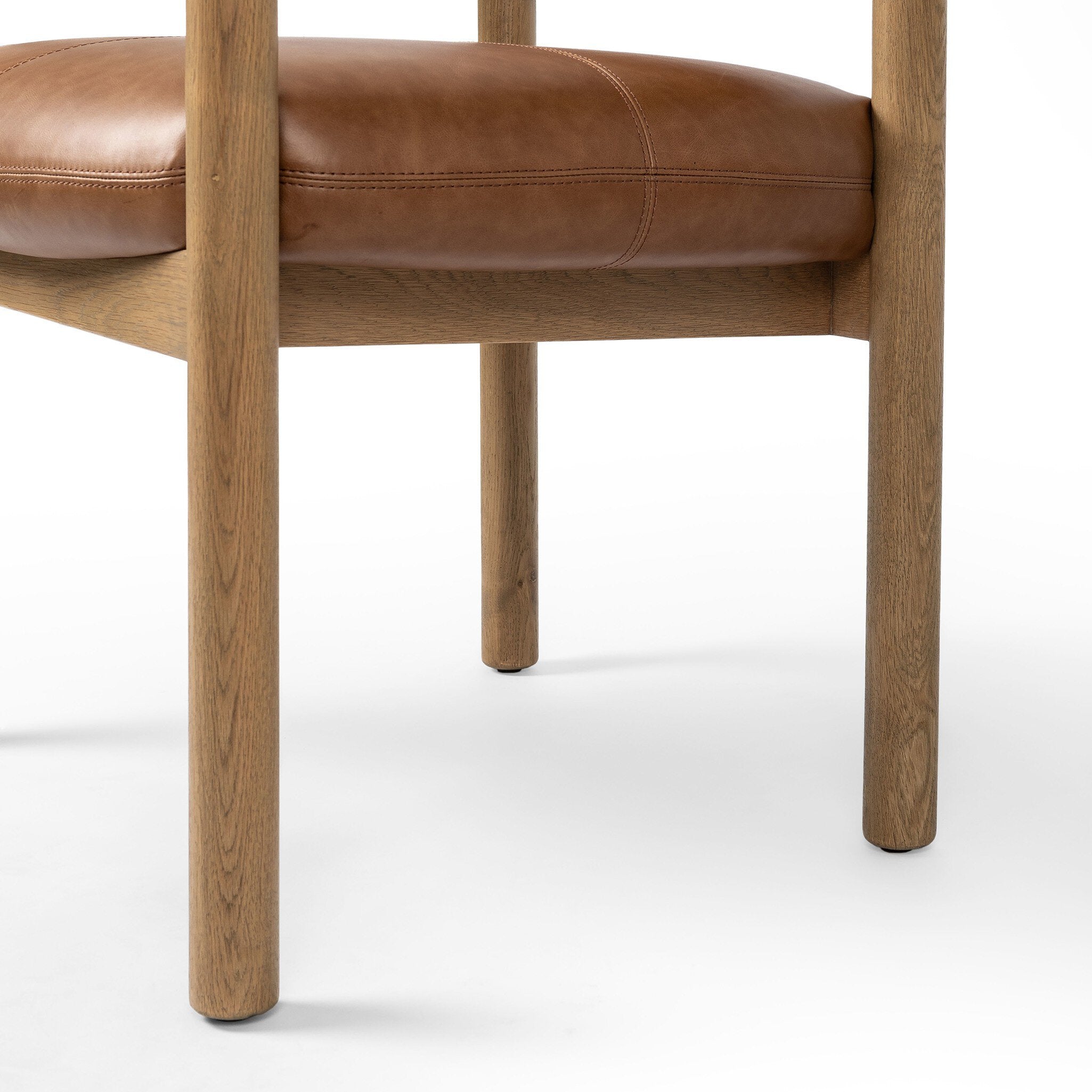 Close up of a brown leather dining armchair with wooden frame on a white background.