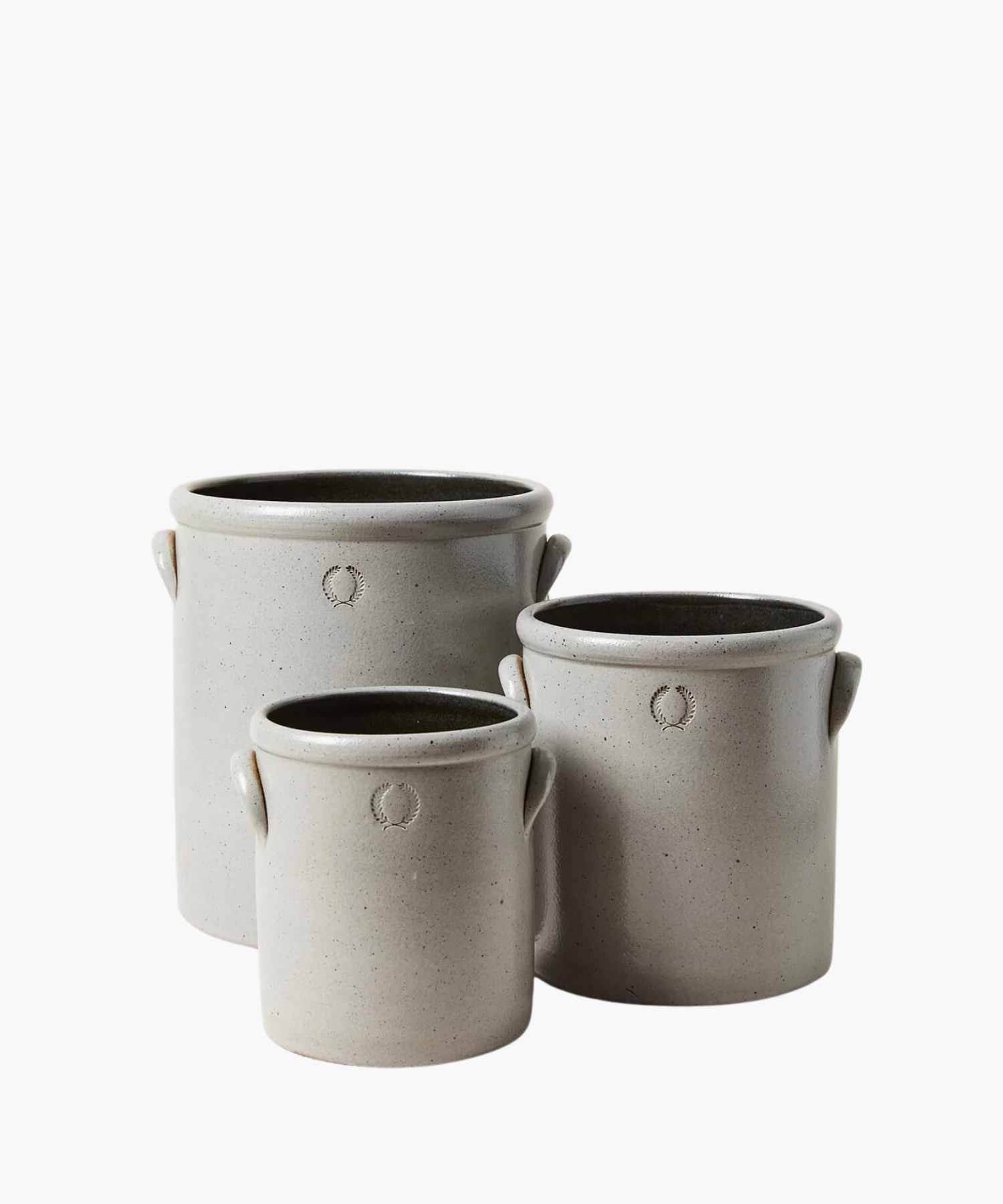 Three gray stoneware crocks of varying sizes with small handles. Each crock has a subtle embossed wreath design, conveying a rustic, artisanal feel. | S.W. Home