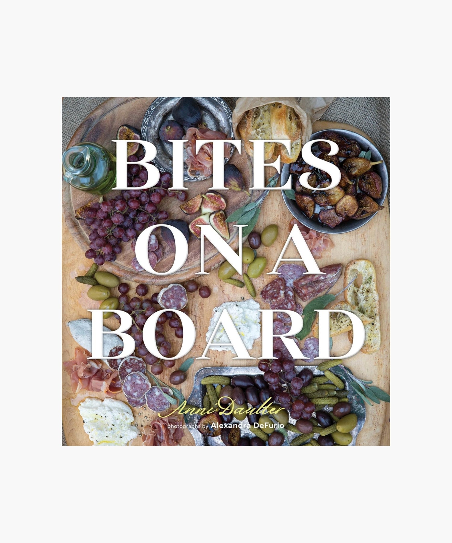 The cover of the book "Bites on a Board" by Anni Dauter featuring a charcuterie board with grapes, olives, figs, cured meats, bread, and cheese. The text "Bites on a Board" overlays the image, evoking a rustic, savory feel. | SW Home