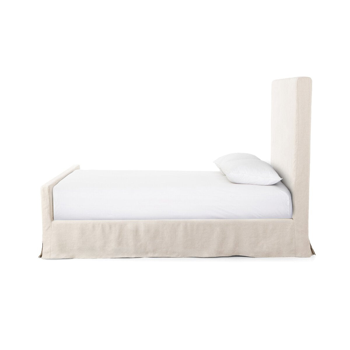 Side profile of a beige slipcover bed with white bedding on a white background.