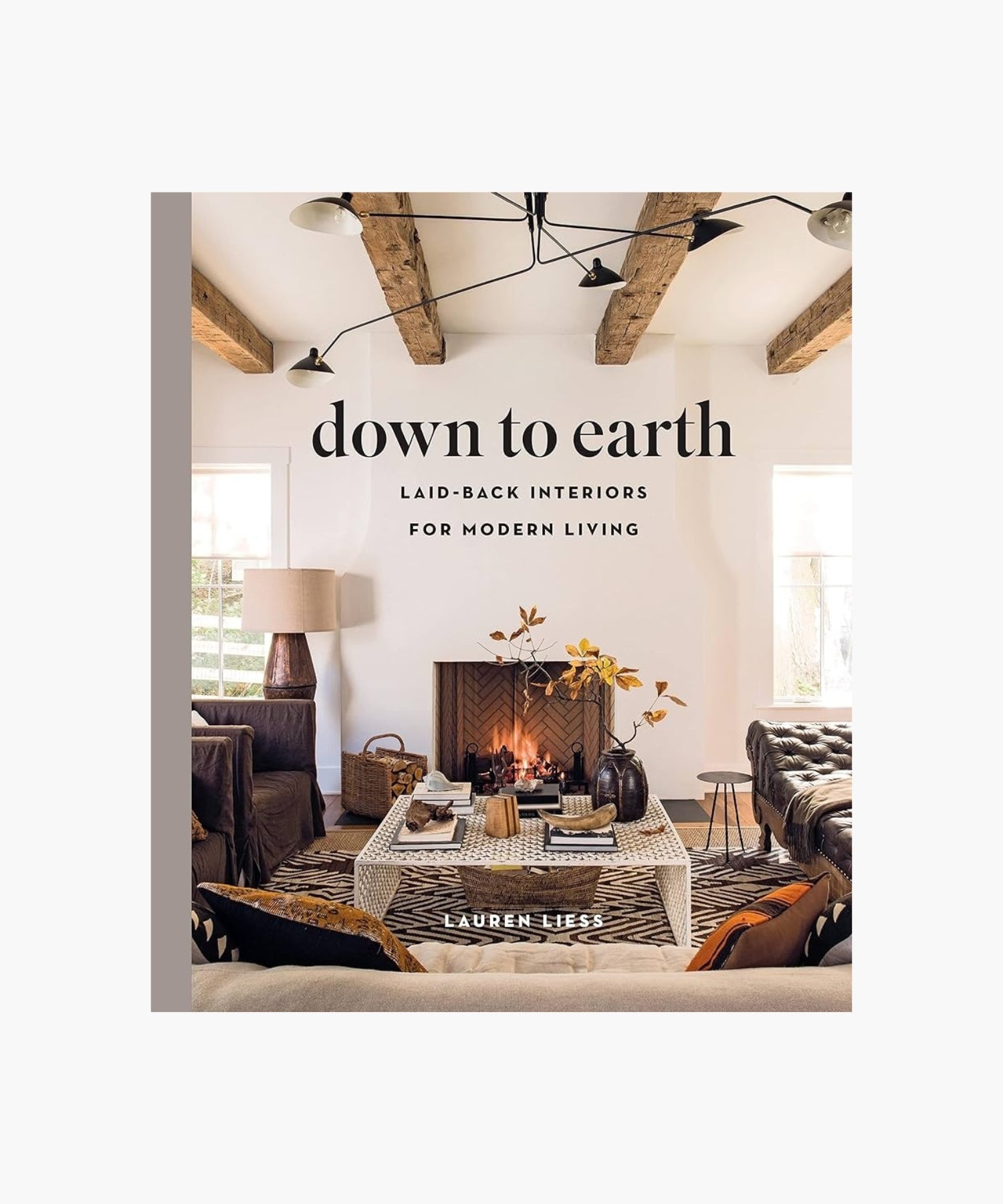 The cover of the book "Down to Earth" by Lauren Liess features a living room with a cozy fireplace, rustic wooden beams, a patterned rug, and modern furniture. The atmosphere is warm and inviting. | S.W. Home