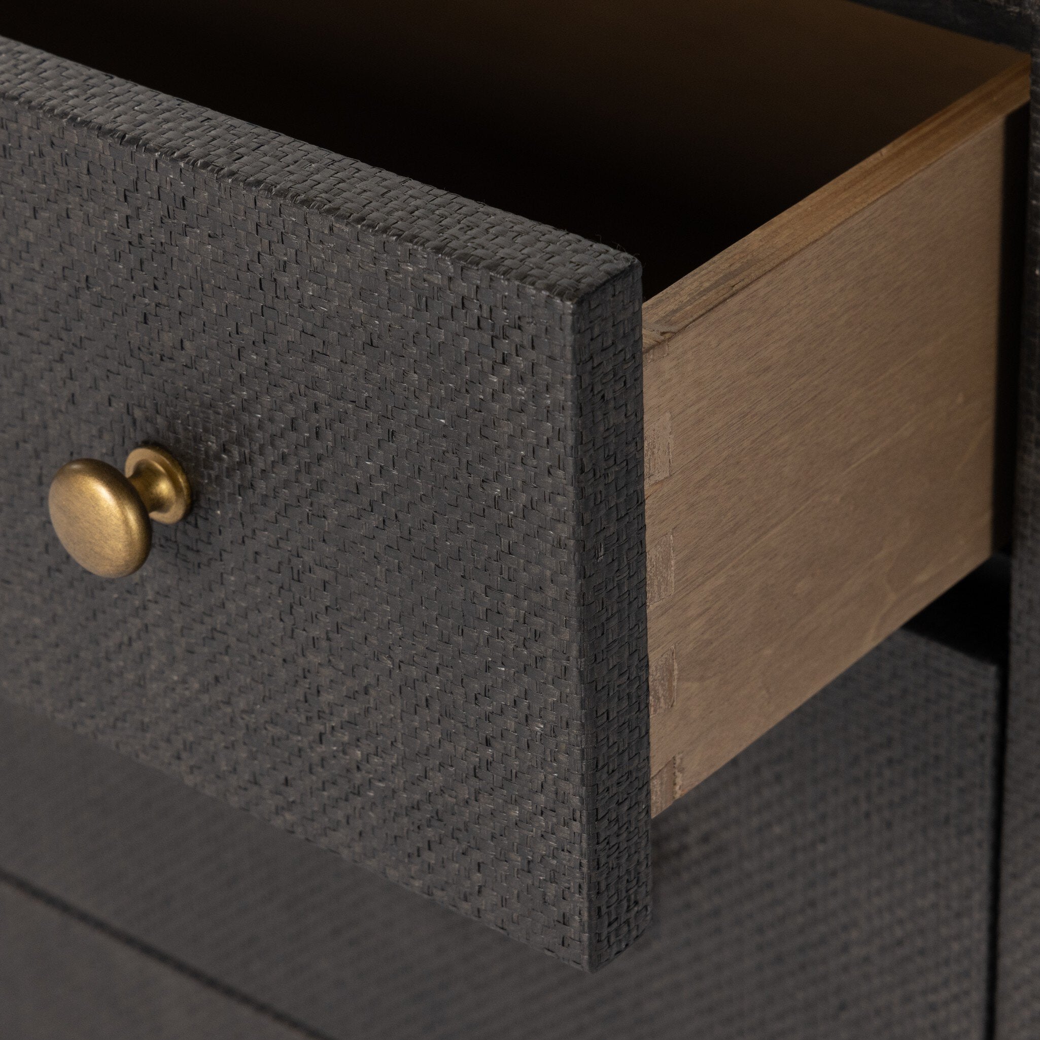 Close up of a black dresser with brass knobs with wooden legs on a white background.