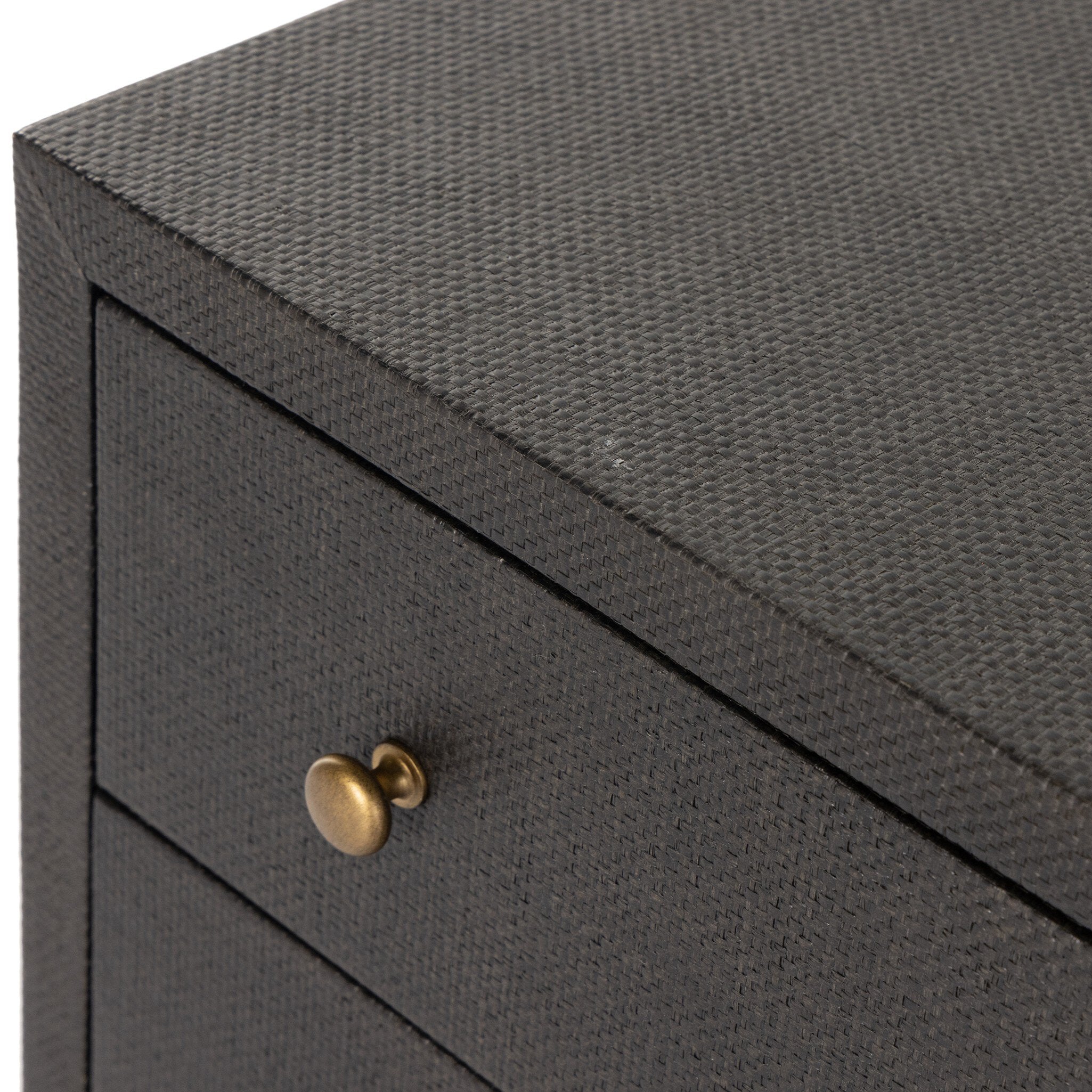 Close up of a black dresser with brass knobs with wooden legs on a white background.