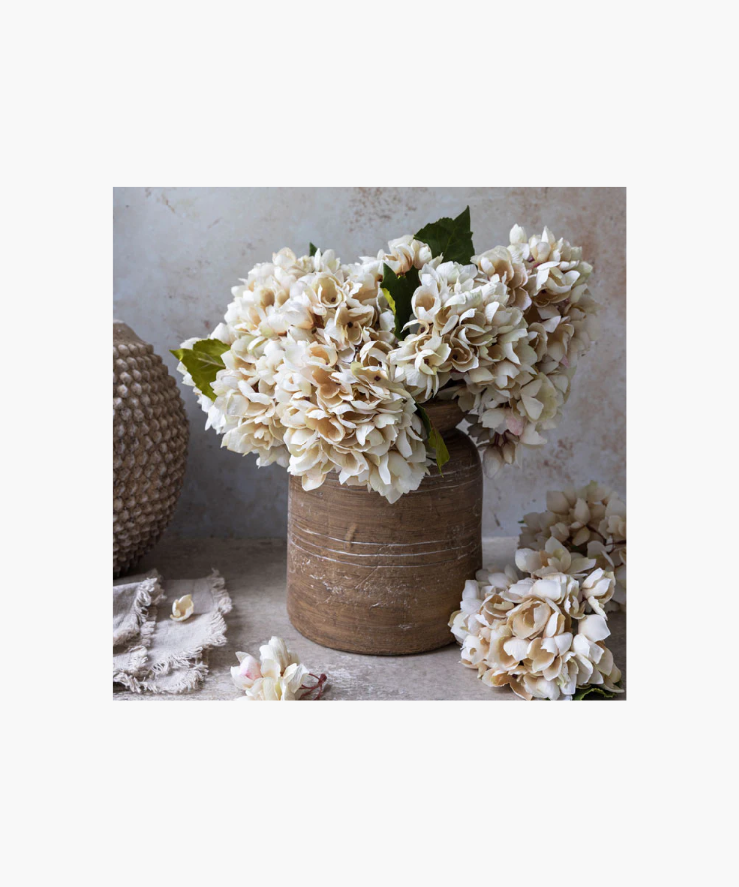A bouquet of light pink hydrangea with lush blossoms and green leaves set in a terracotta pot, conveying a sense of delicate beauty. | SW Home