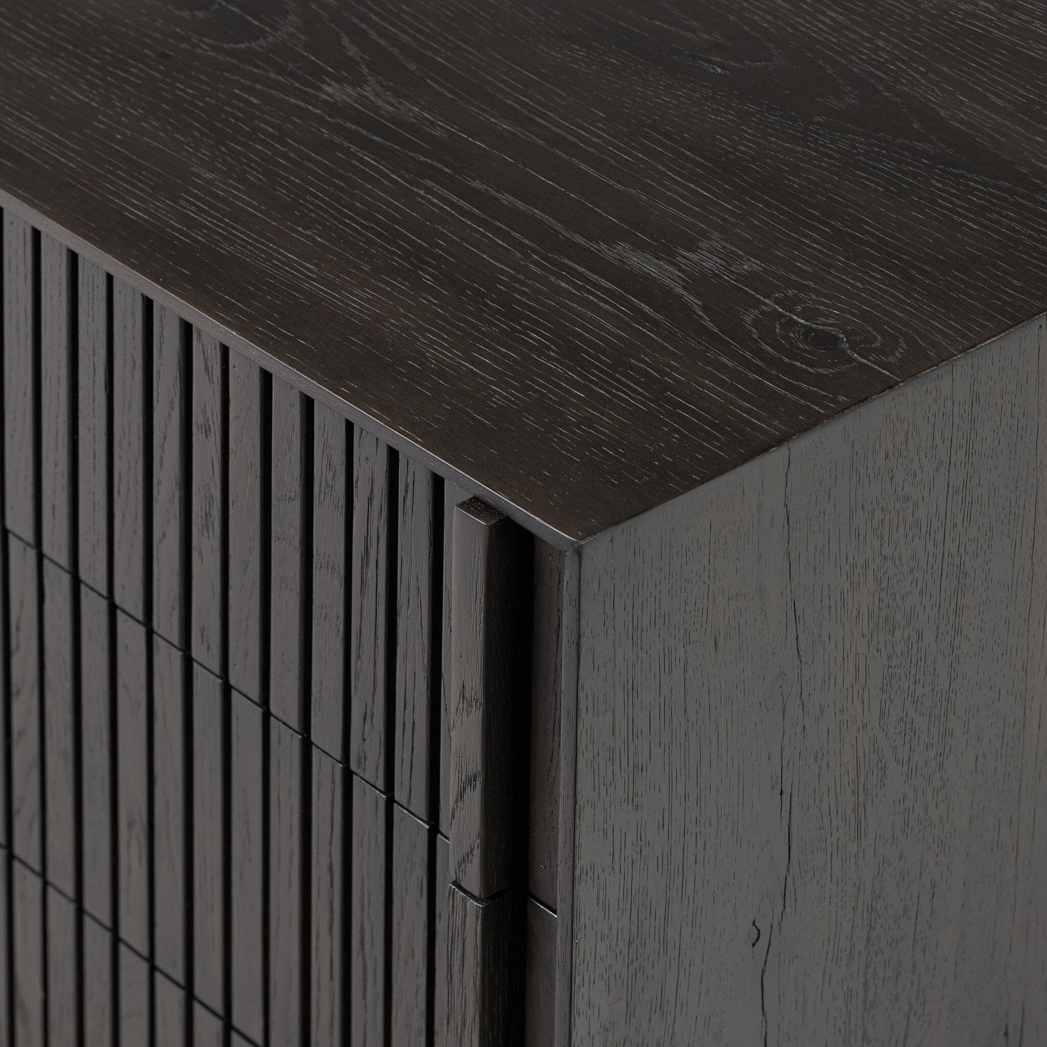 Close up of a dark wooden dresser with vertical reed detailing and three drawers on a white background.