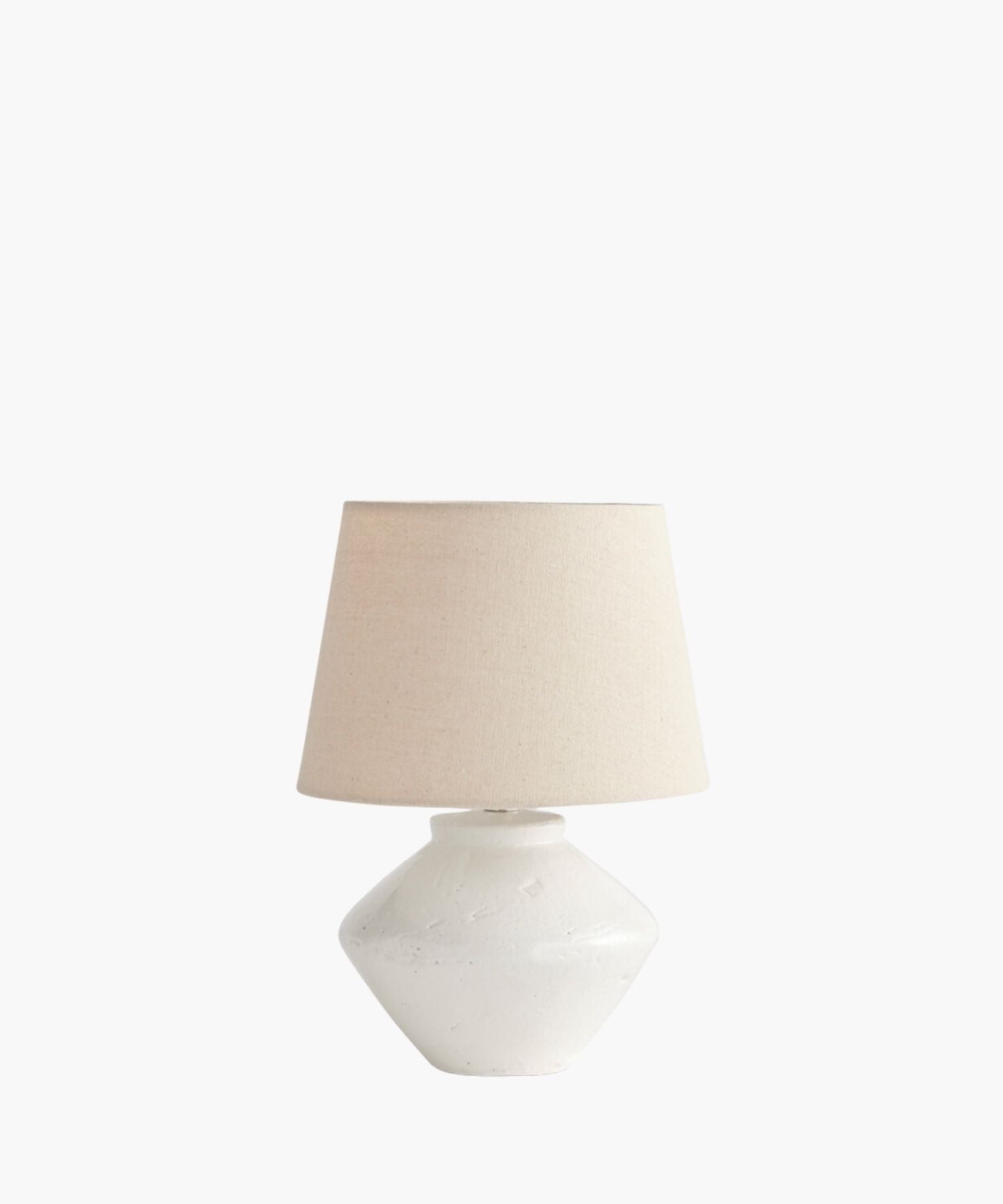 A cream table lamp with a textured, wide ceramic base and a simple fabric shade. The lamp's minimalist design evokes a calm and neutral tone. | S.W. Home