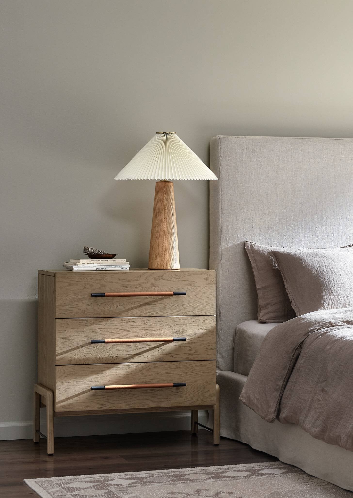 Wooden nightstand with lamp next to a bed in a bedroom setting
