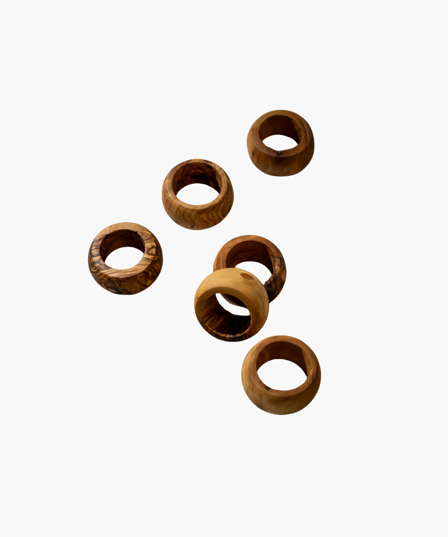 Six wooden napkin rings with varied natural grain patterns are scattered on a plain white background, showcasing a rustic and earthy aesthetic. | S.W. Home
