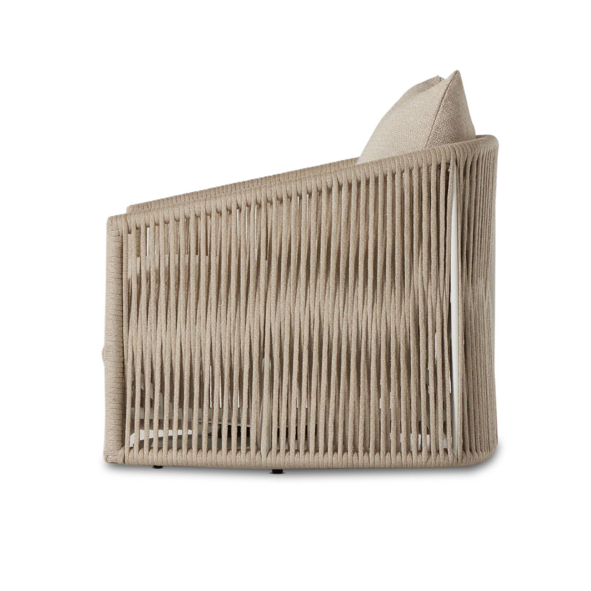 A side profile of a rope based-designed swivel chair in a sand color with a wide cushion and throw pillow on a white background. 