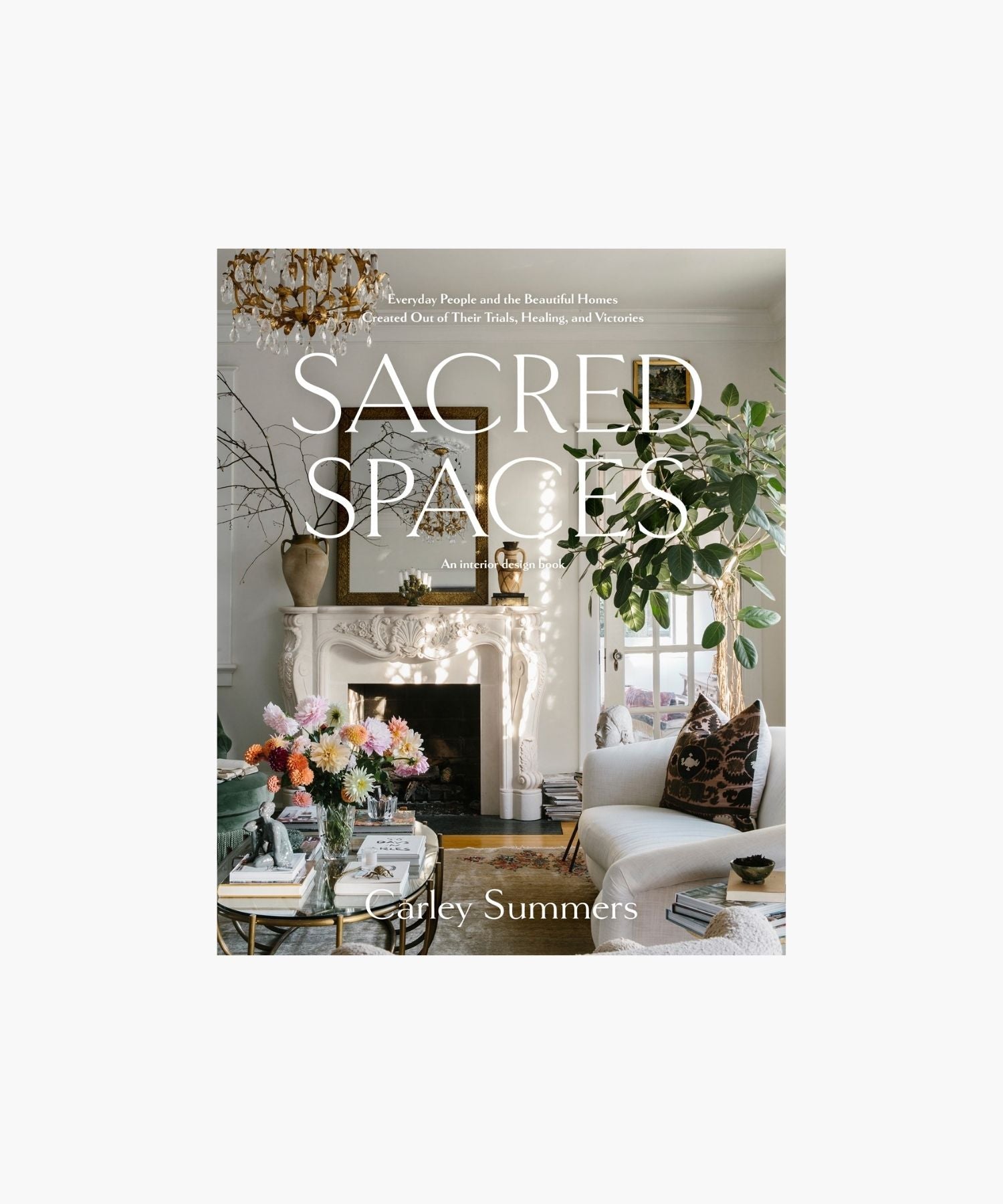 The cover of the book "Sacred Spaces" by Carley Summers featuring a cozy living room with elegant decor; a white fireplace, chandelier, vibrant flowers, and lush greenery create a tranquil, inviting ambiance. | S.W. Home