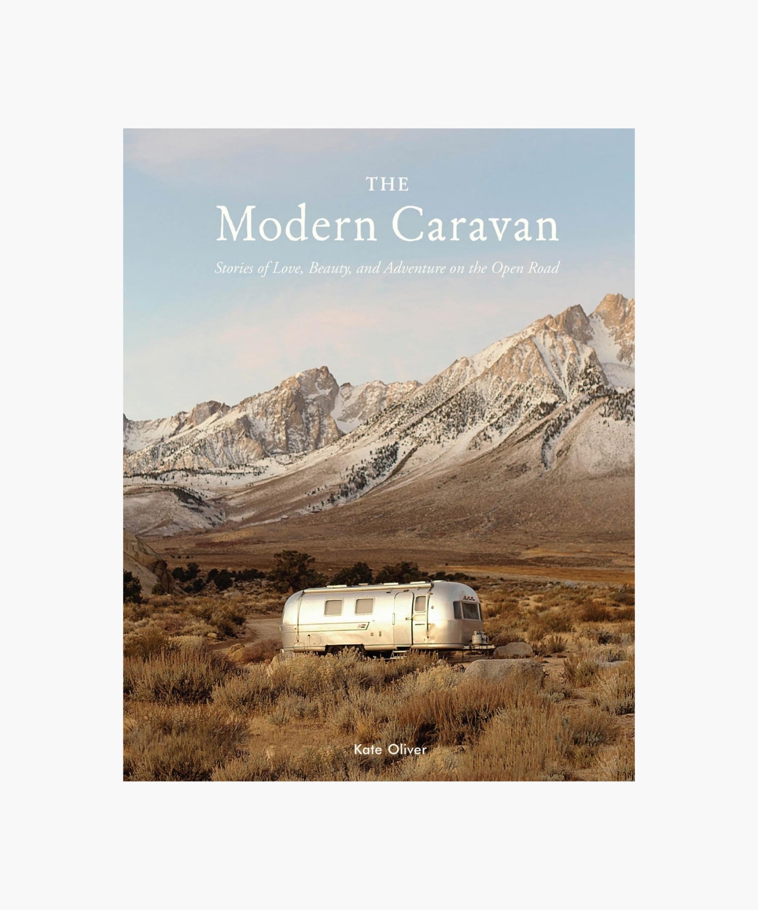 The cover of the book "The Modern Caravan" by Kate Oliver featuring a shiny silver RV in a vast, desolate landscape with rugged mountains in the background, conveying adventure. | S.W. Home