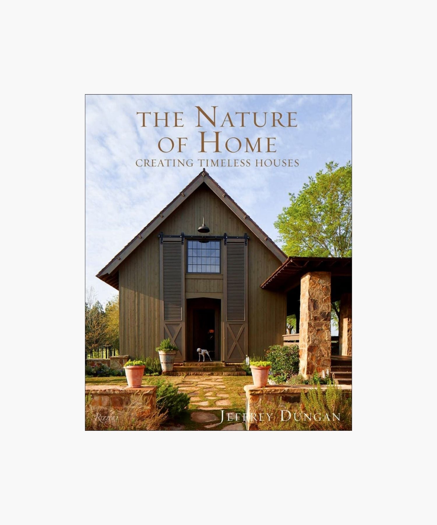 The cover of the book "The Nature of Home" by Jeffrey Dungan, featuring a rustic house with wooden siding, large windows, stone pillars, and surrounding greenery under a clear sky. | S.W. Home