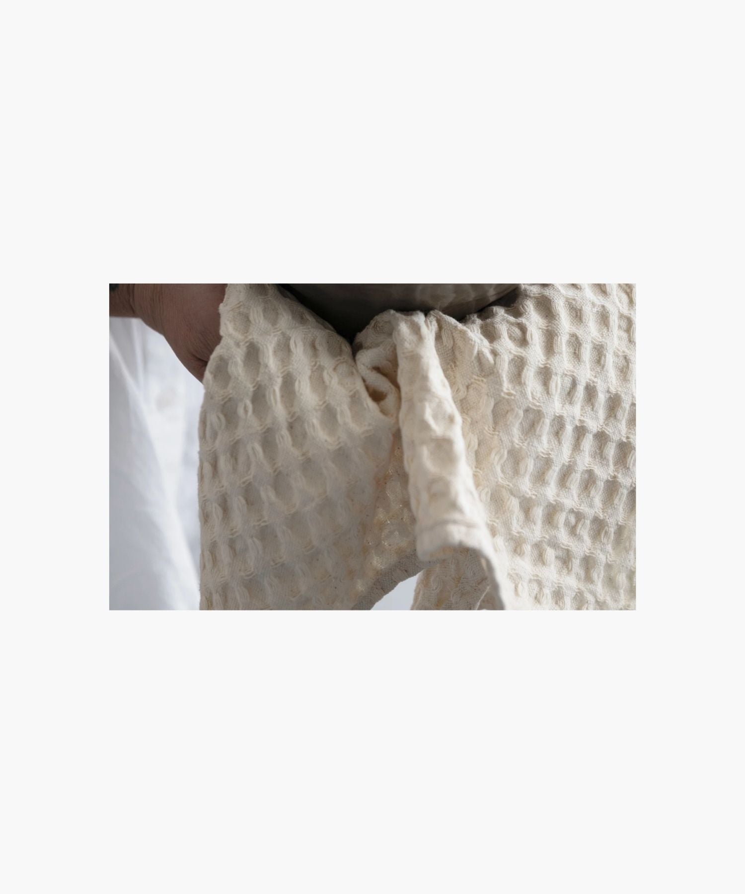 A close up picture of a cream colored, rectangular waffle-weave tea towel highlighting the texture and a clean, simple appearance.